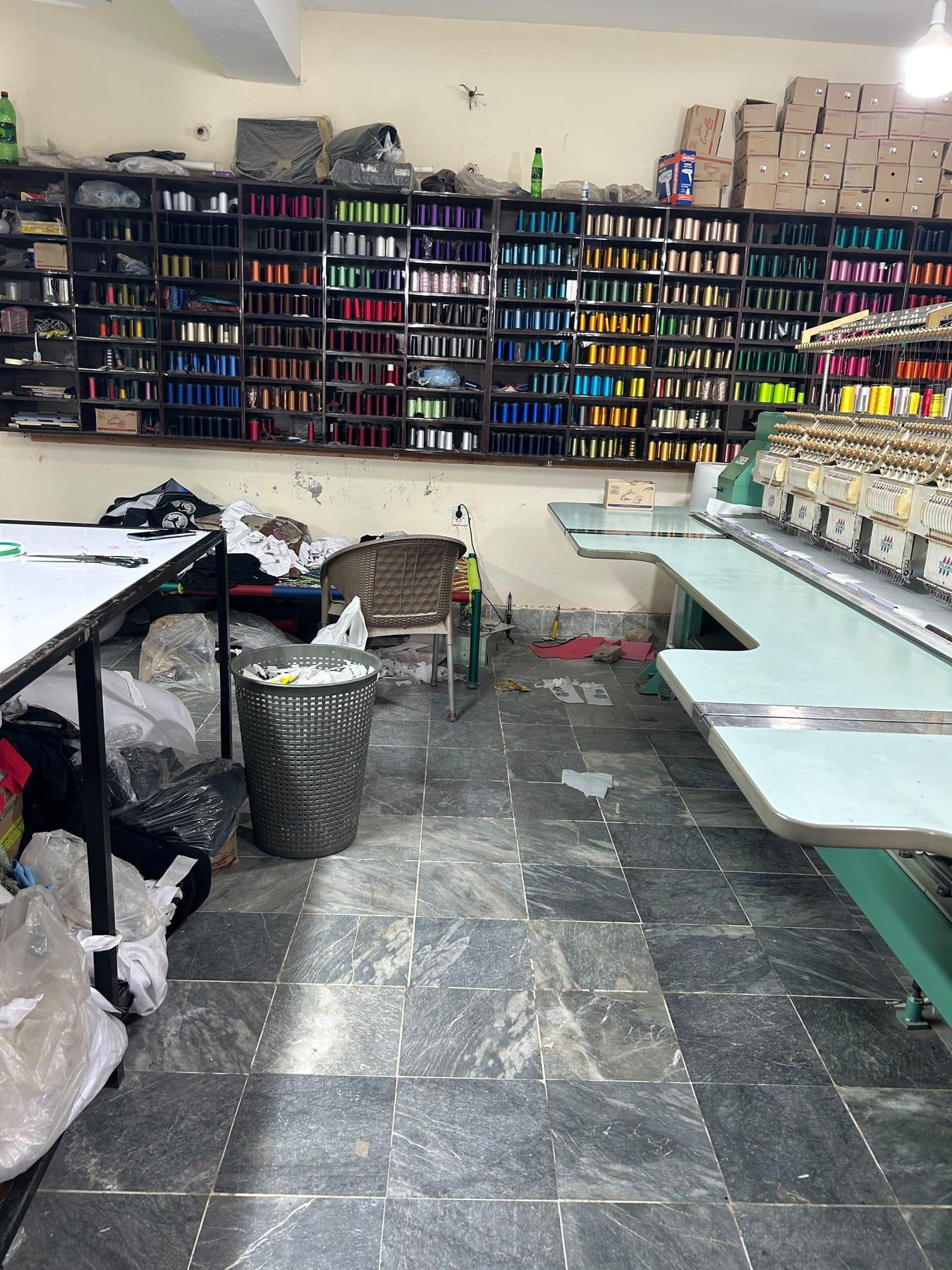 A wall of shelves holding embroidery thread cones in hundreds of colours beside the embroidery machine