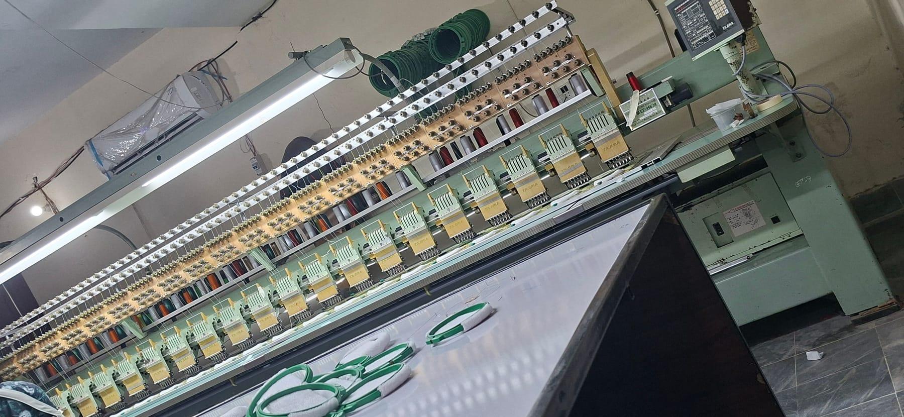 A long Tajima multi-head embroidery machine with a row of stitching heads, thread cones above and green hoops on the table